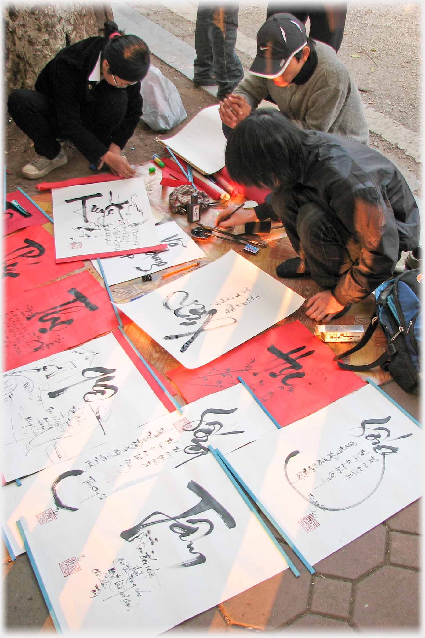 Hunkered writer beside woman prepariing sheets of calligraphy.