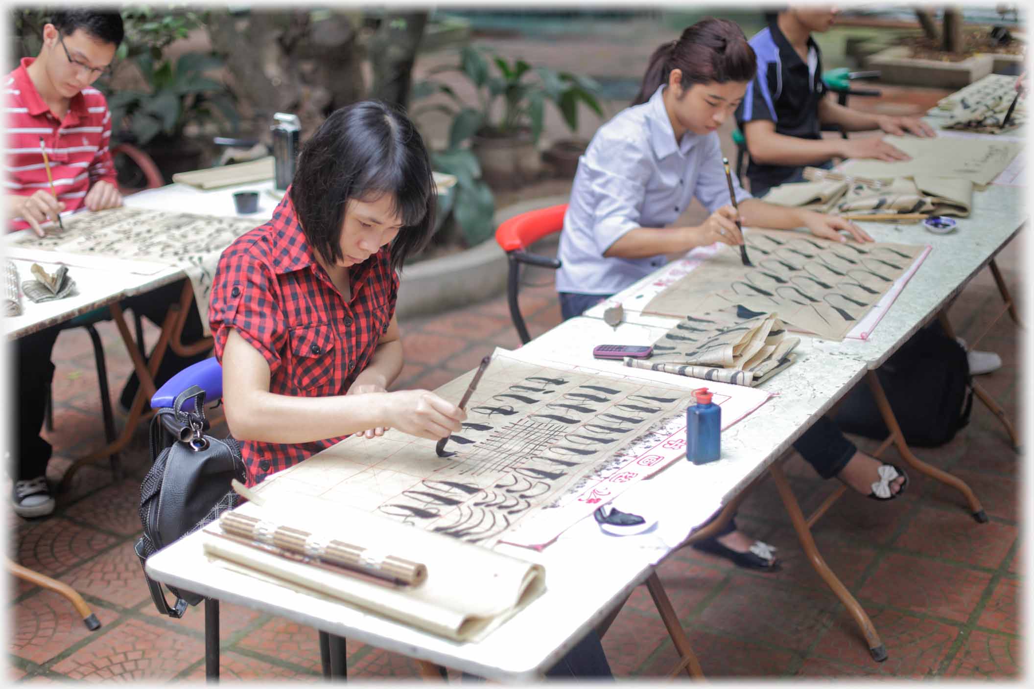 Two women at tables writing repetitive marks with brush.