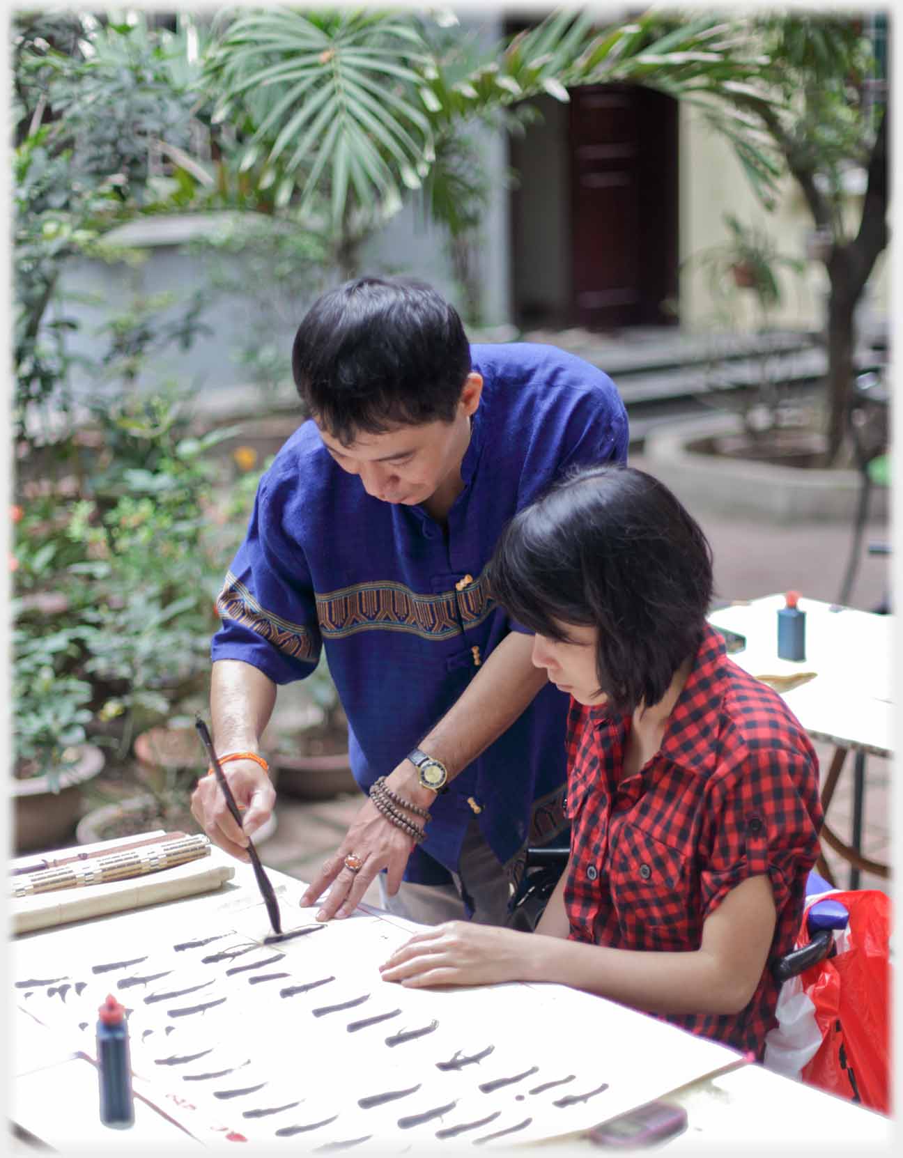 Teacher standing beside seated pupil demonstrating with brush.