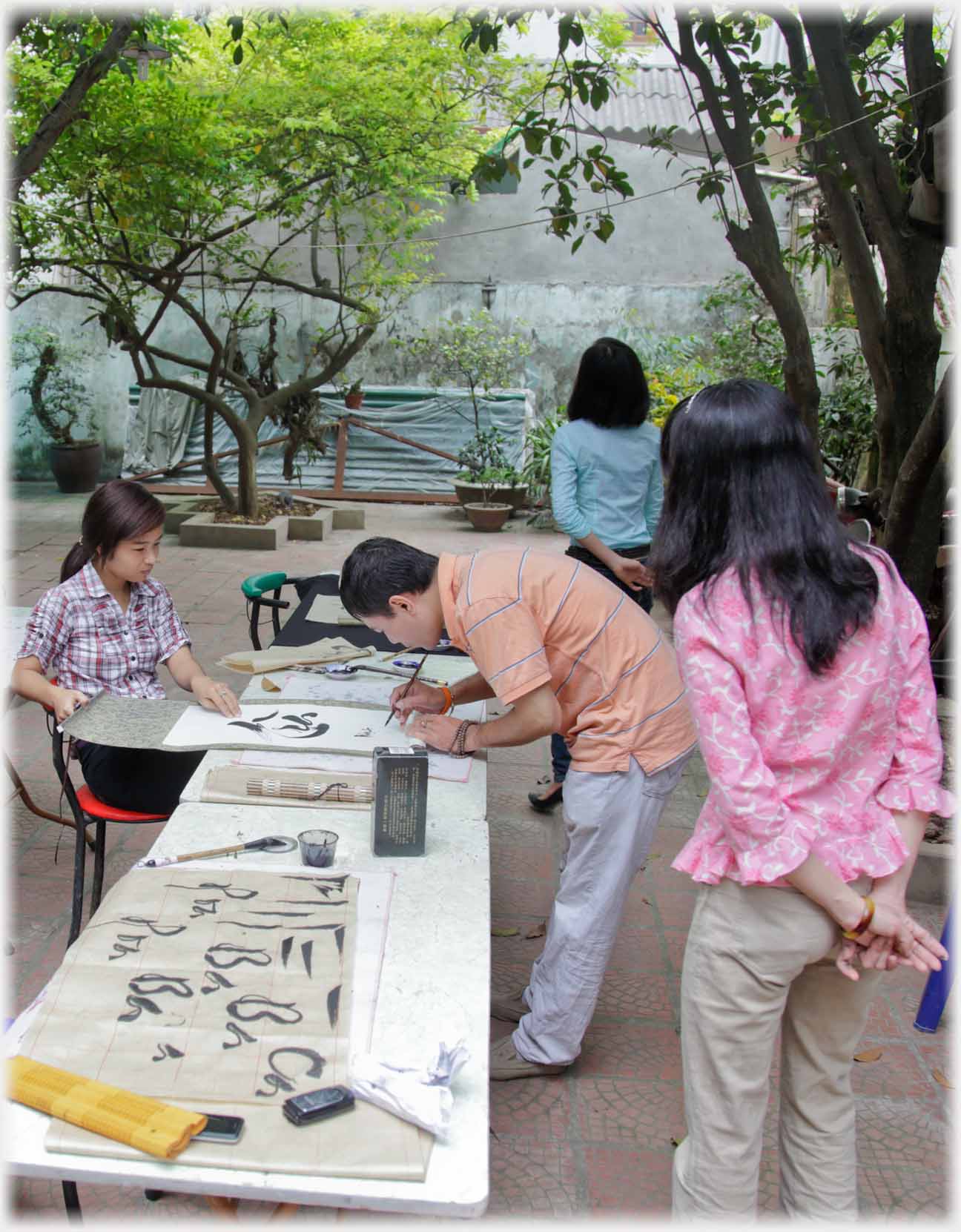 Man bending over table writing with brush, pupils watching.