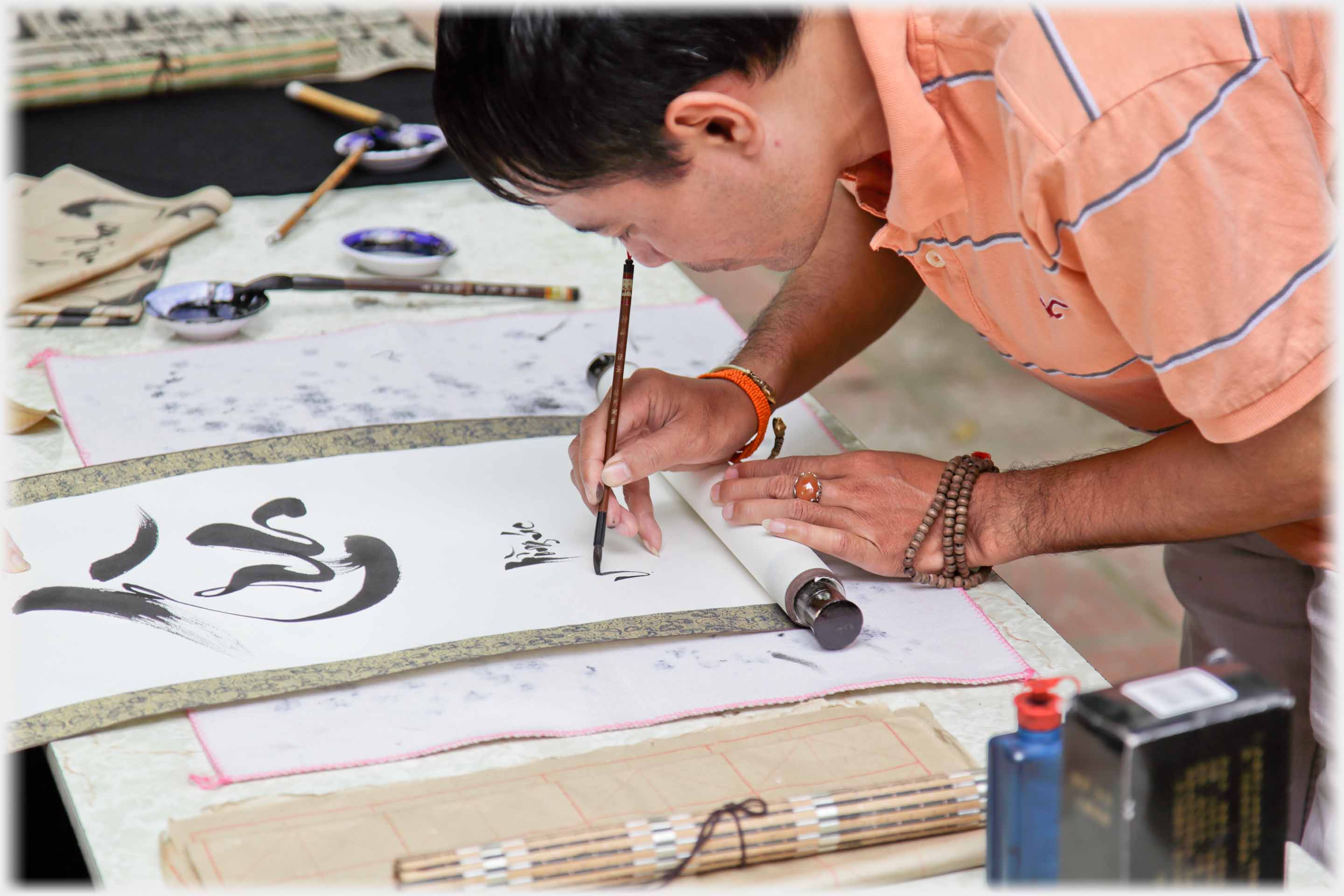 Close shot of teacher writing with fine brush from side.