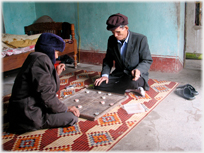 Two men sitting on floor in coats and hats playing chess.