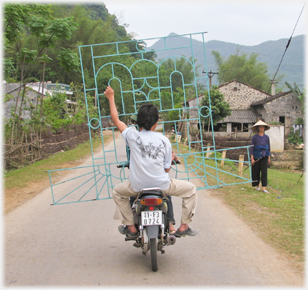 Pillion holding large grill, woman walking.