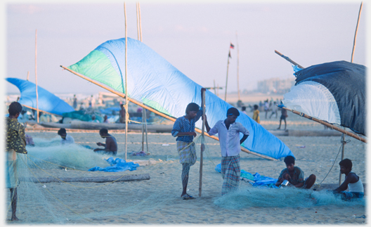 Men sitting mending nets others talking to them as sun sets.