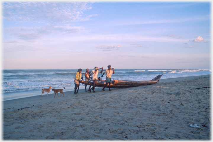 Men maneavering  boat up the beach.