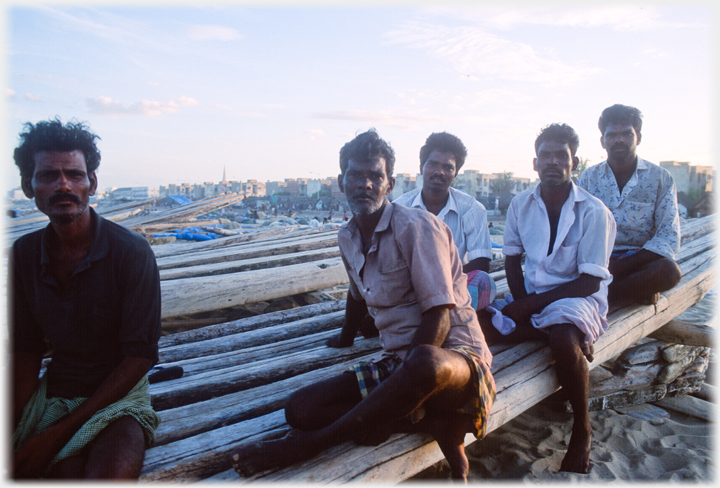 Five men sitting on boat logs looking at camera.