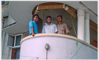 Three men smiling broadly on balcony.