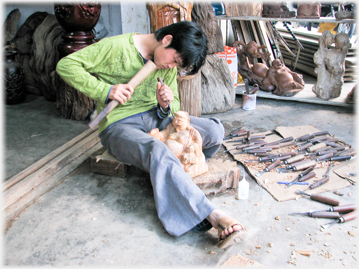 Intent wood carver with profusion of chisels laid out beside him.