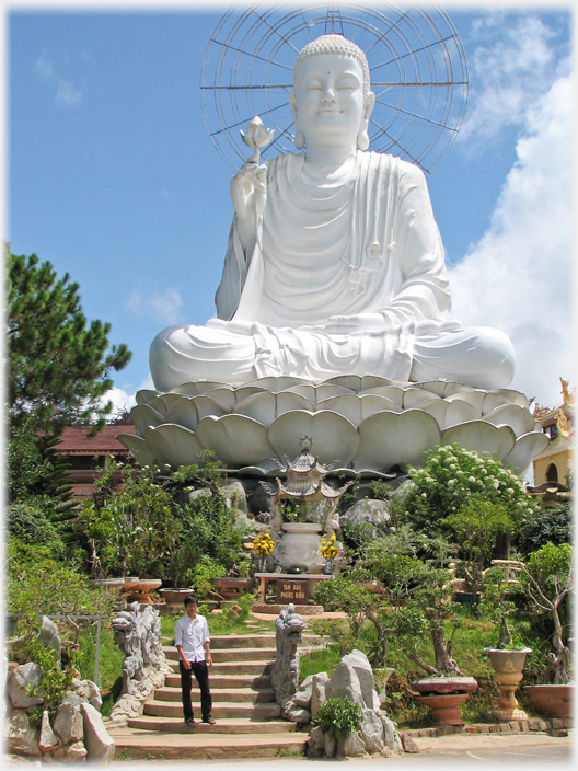 Large white sitting Buddha above garden and steps.