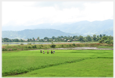 Five distant figures with water, a village and hills for background.