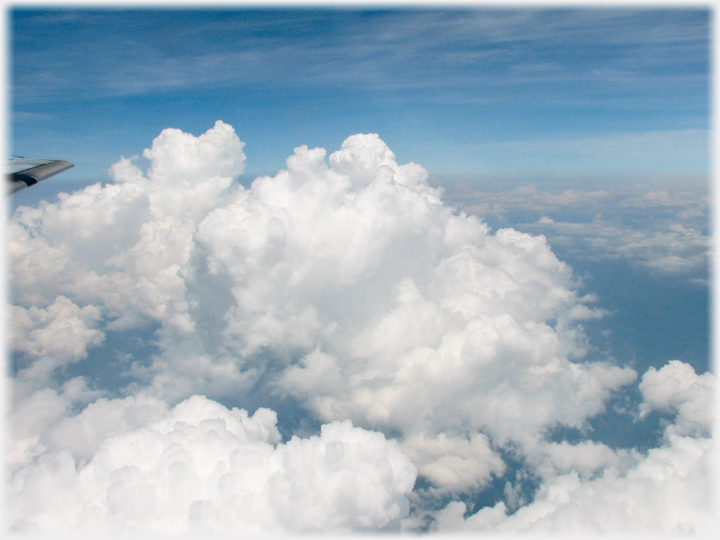 Large cumulous cloud rising up to height of plane wing tip.