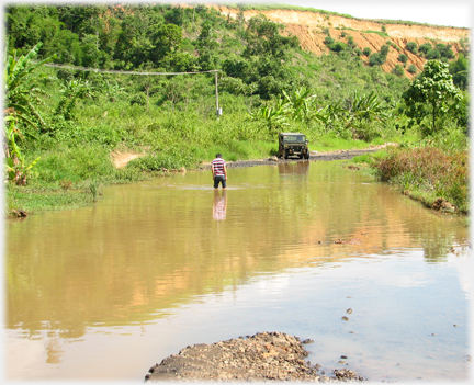 Han wading through river, Jeep parked on bank.