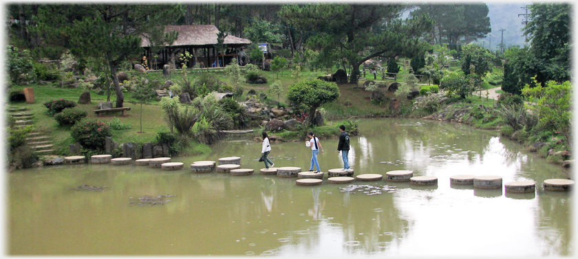 Three people walking over the stepping stones.