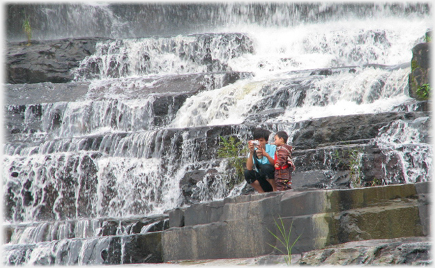 Water pouring over and down rocks in step formation, Han and Sach on steps by water.