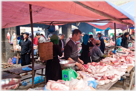 Butcher and his meat and woman with basket.