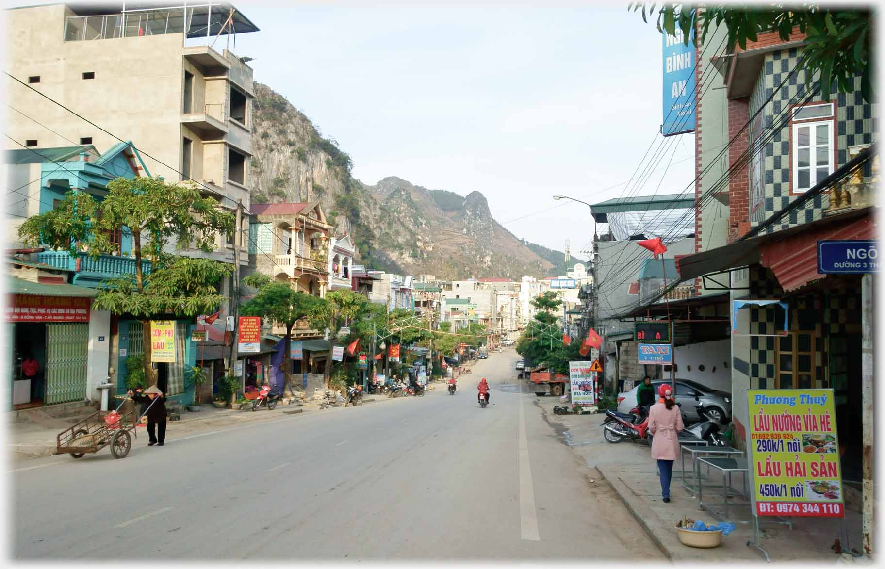 Wide streeet with no cars, a few people and motorbikes.