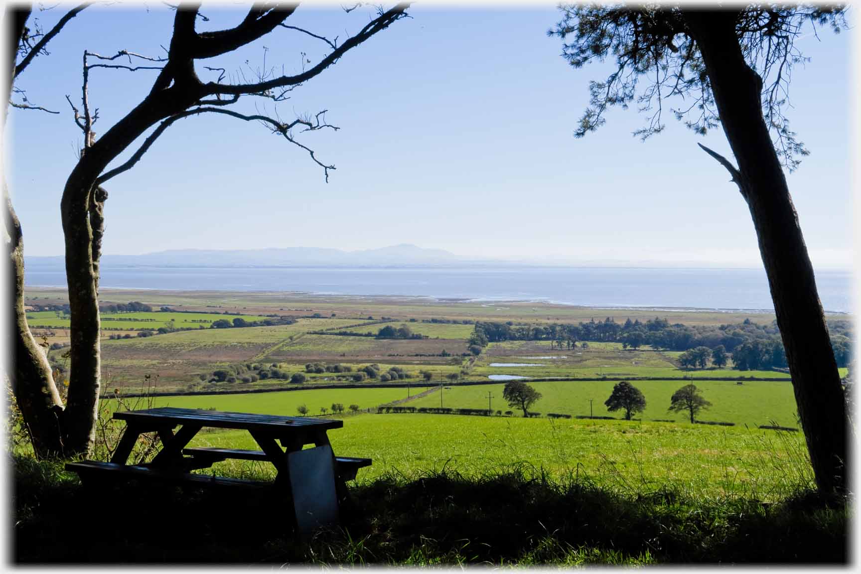 Picnique bench framed with view to sea across hills.
