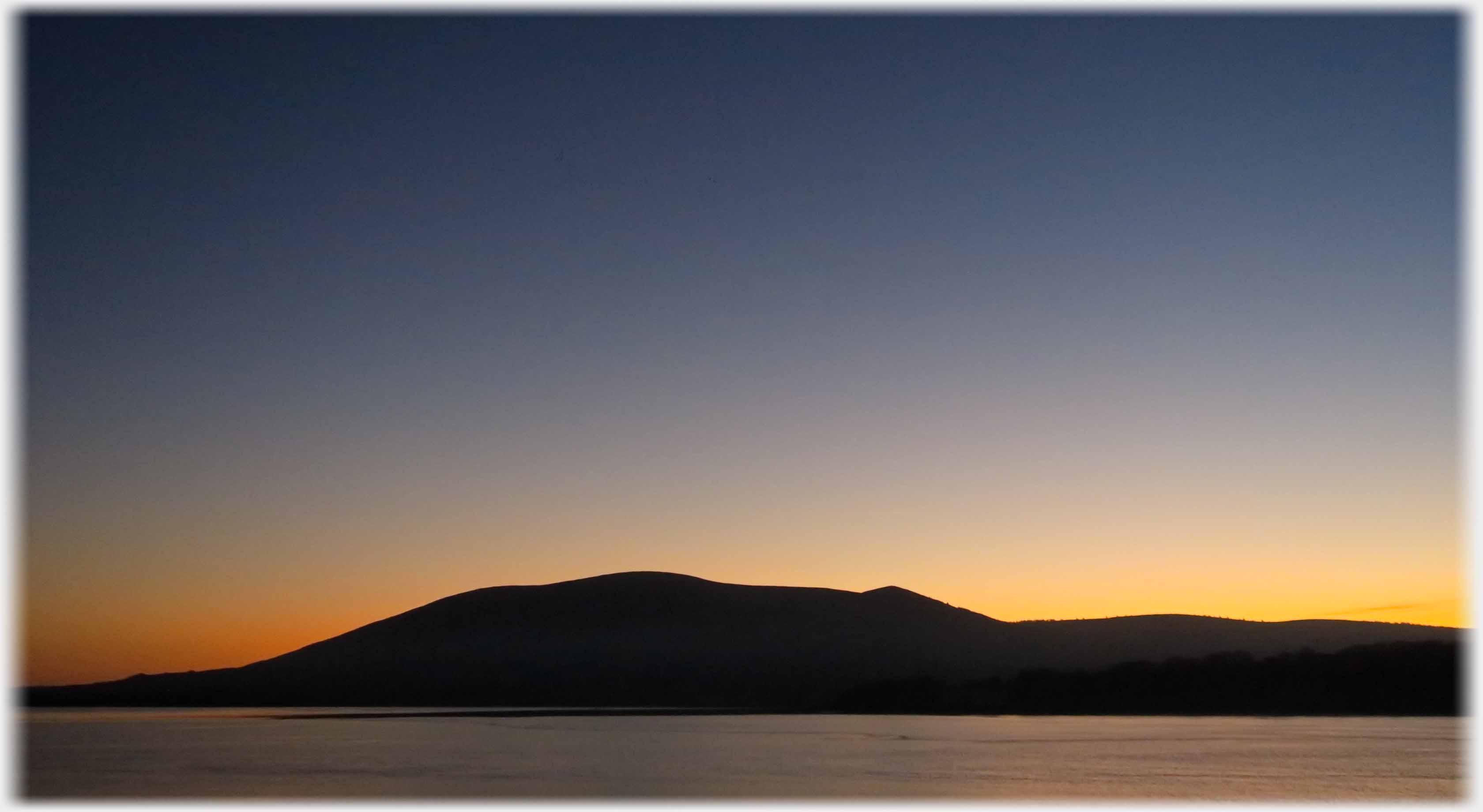 Silhouetted hill against orange sky.