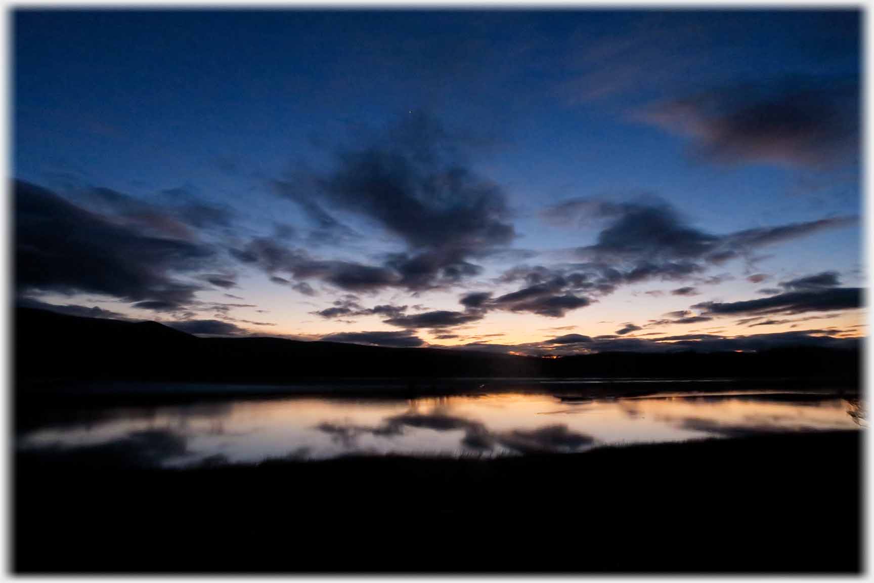End of sunset with clouds reflected in water.