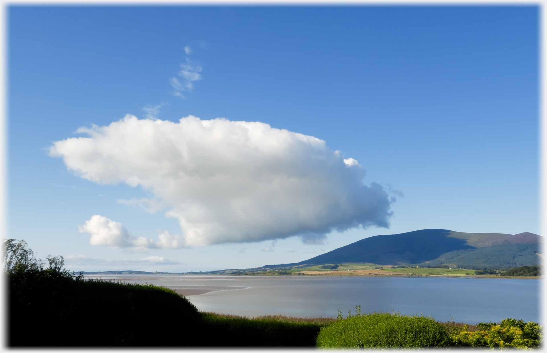 Large cloud dwarfing hill.