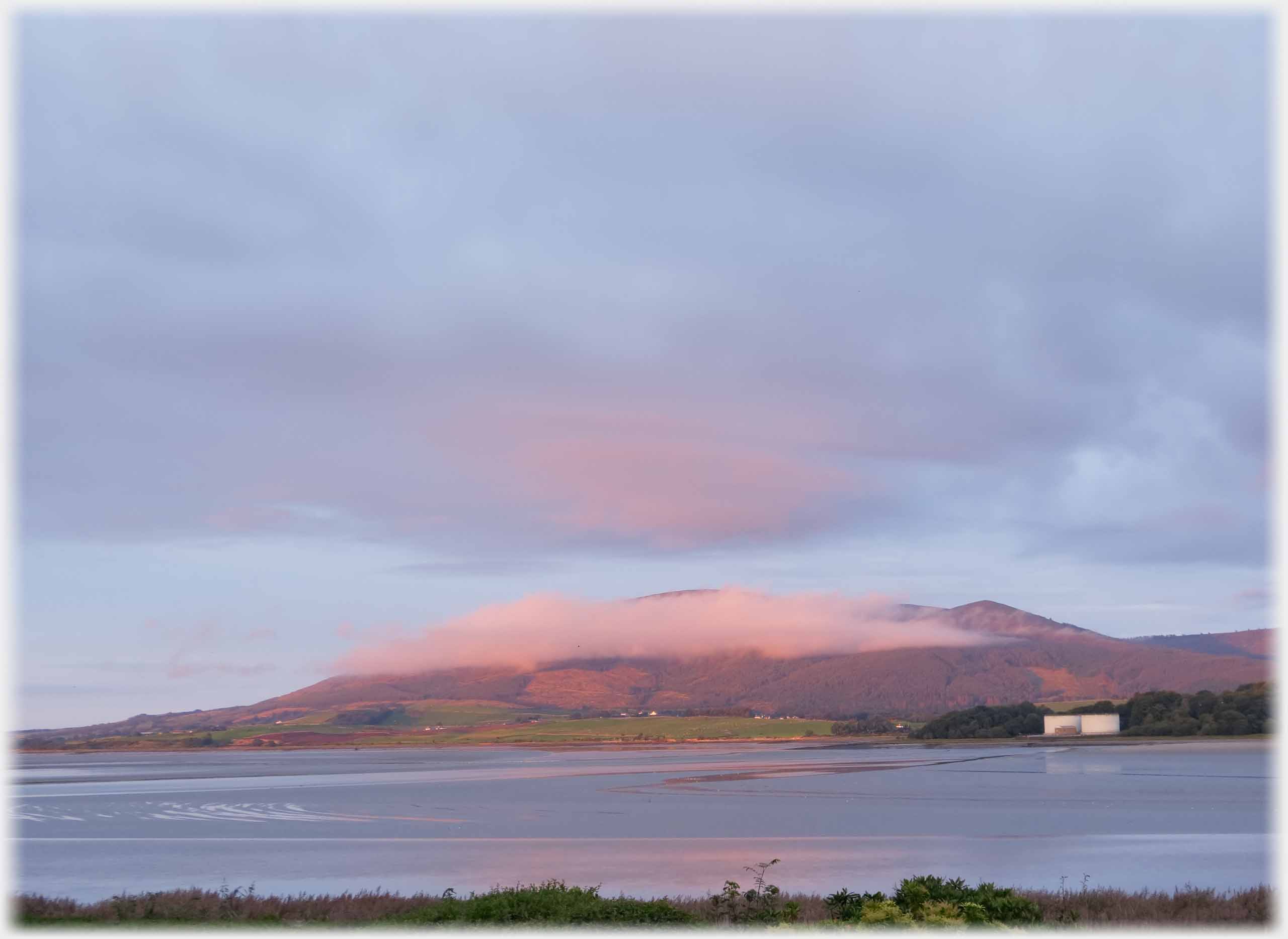 Hill with pink cloud clinging to it, foreground sea.