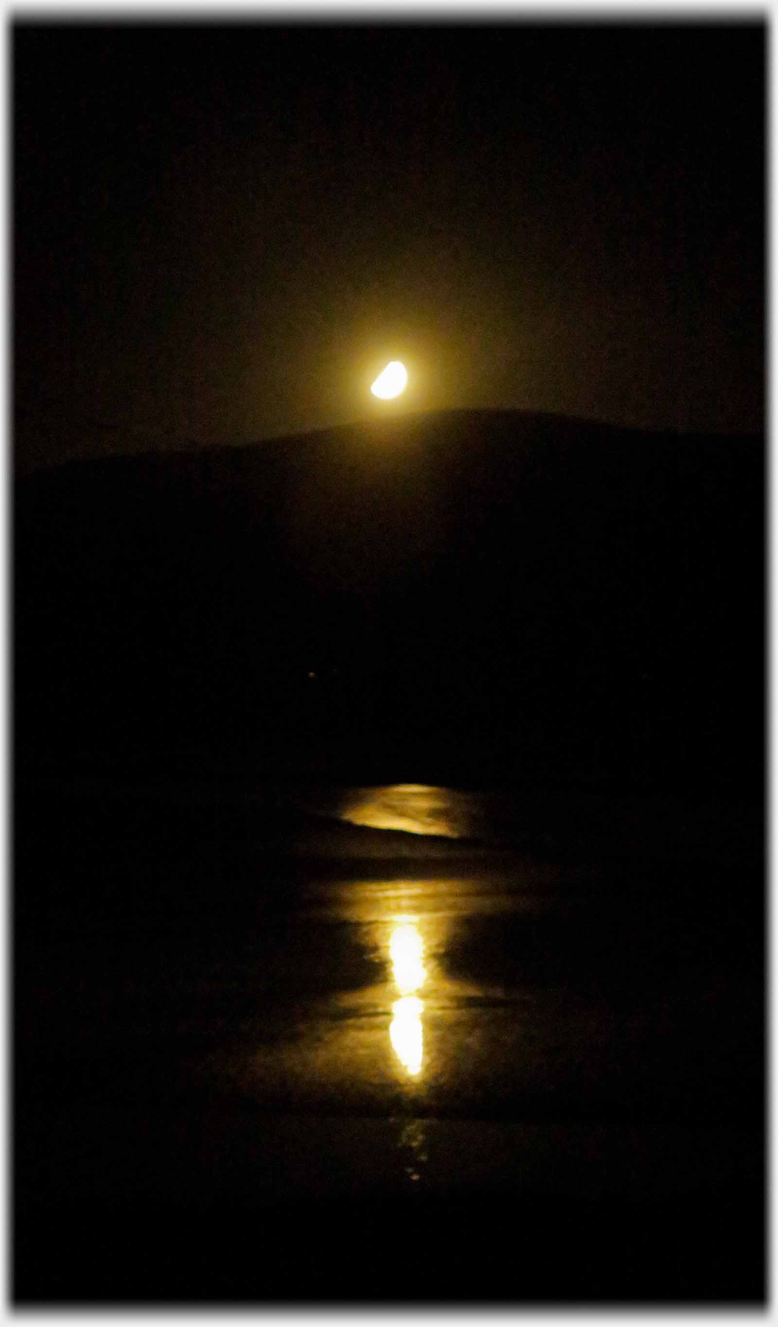 Moon reflected just over black hill outline.