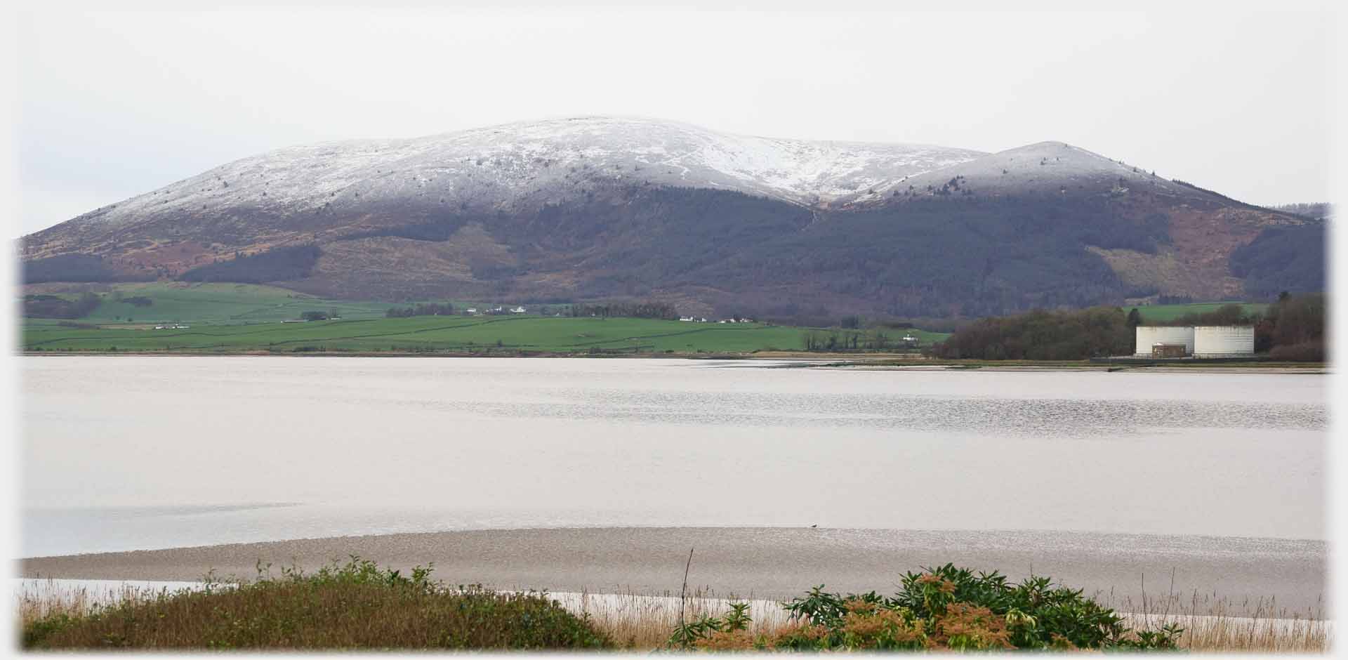 Overcast hill and water with snow on hilltop.