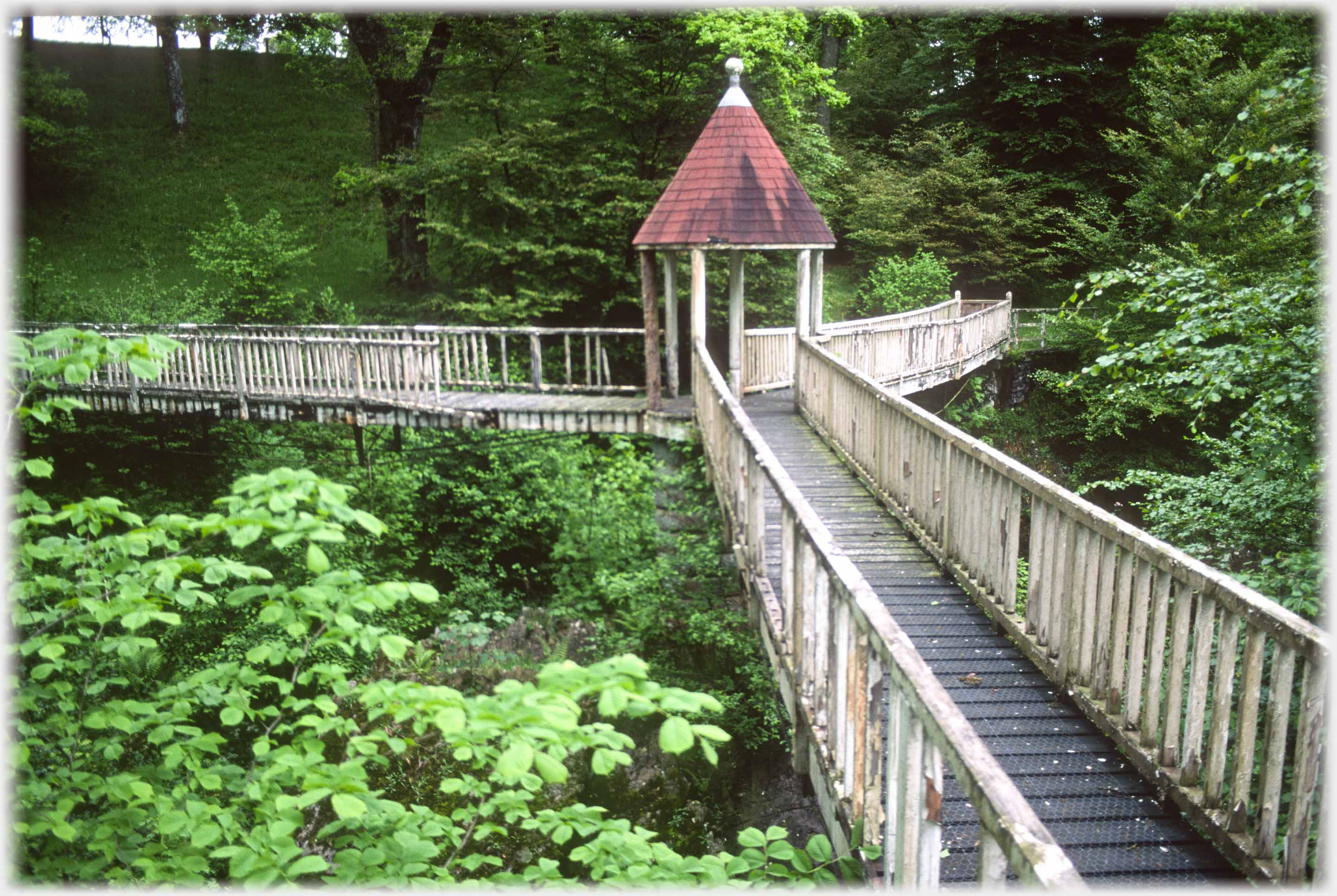 Three balustraded walkways meeting at central roofed point, trees underneath.