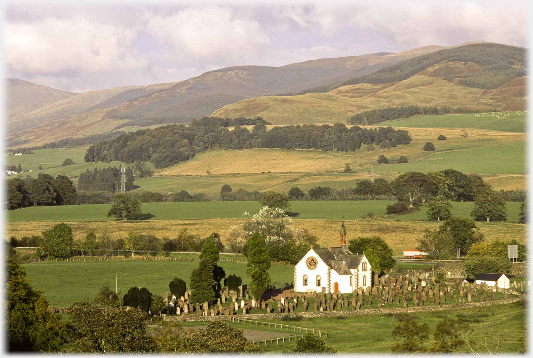 Church in graveyard, fields and hills behind.