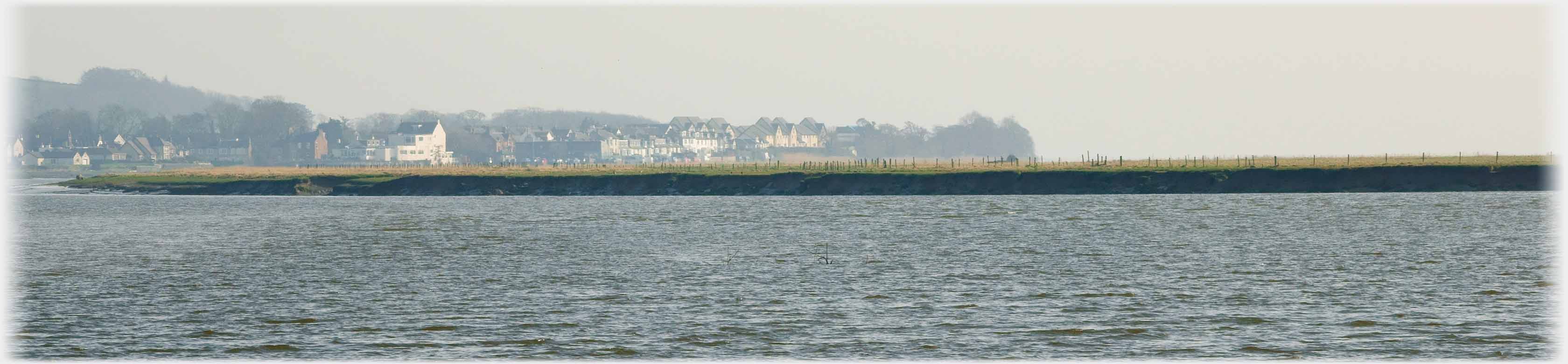 Water with dark bank and houses above in the distance.