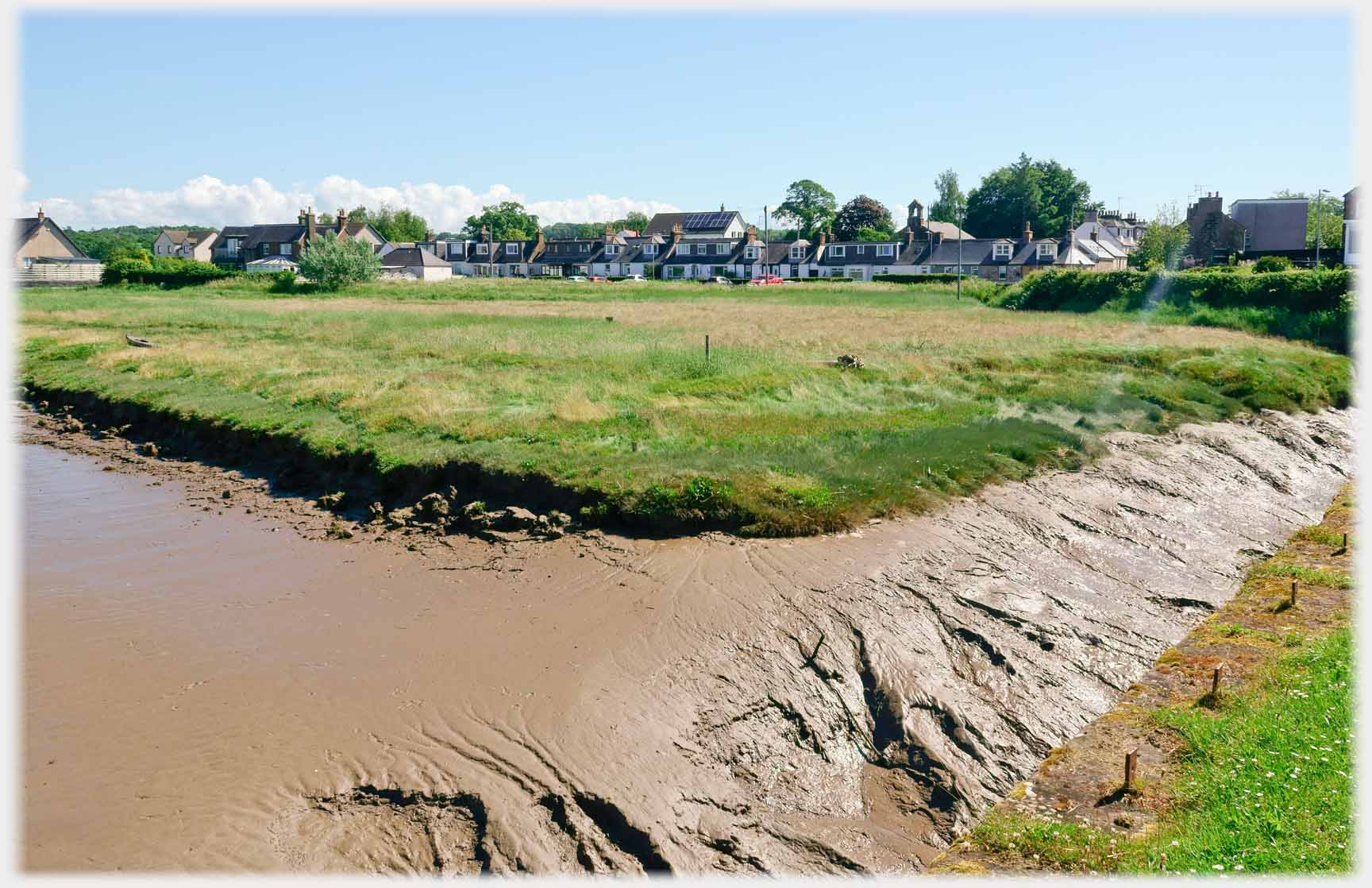 Mud banks, field and distant row of houses.