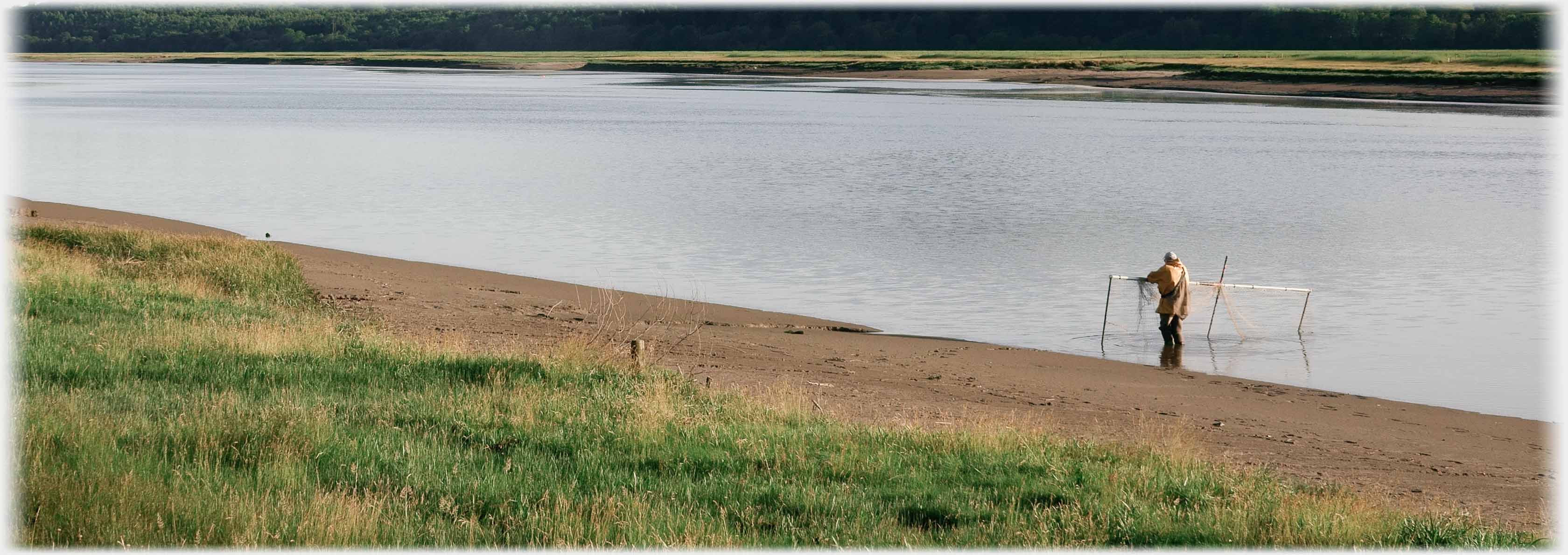 Man standing in river with net on poles.