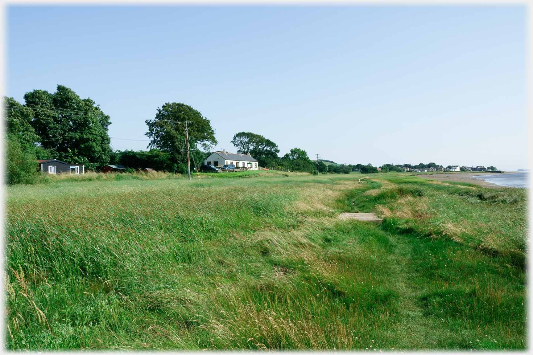 Wide grass river side with distant houses anad one house nearer.