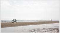 Bike standing on sandbar, man walking.