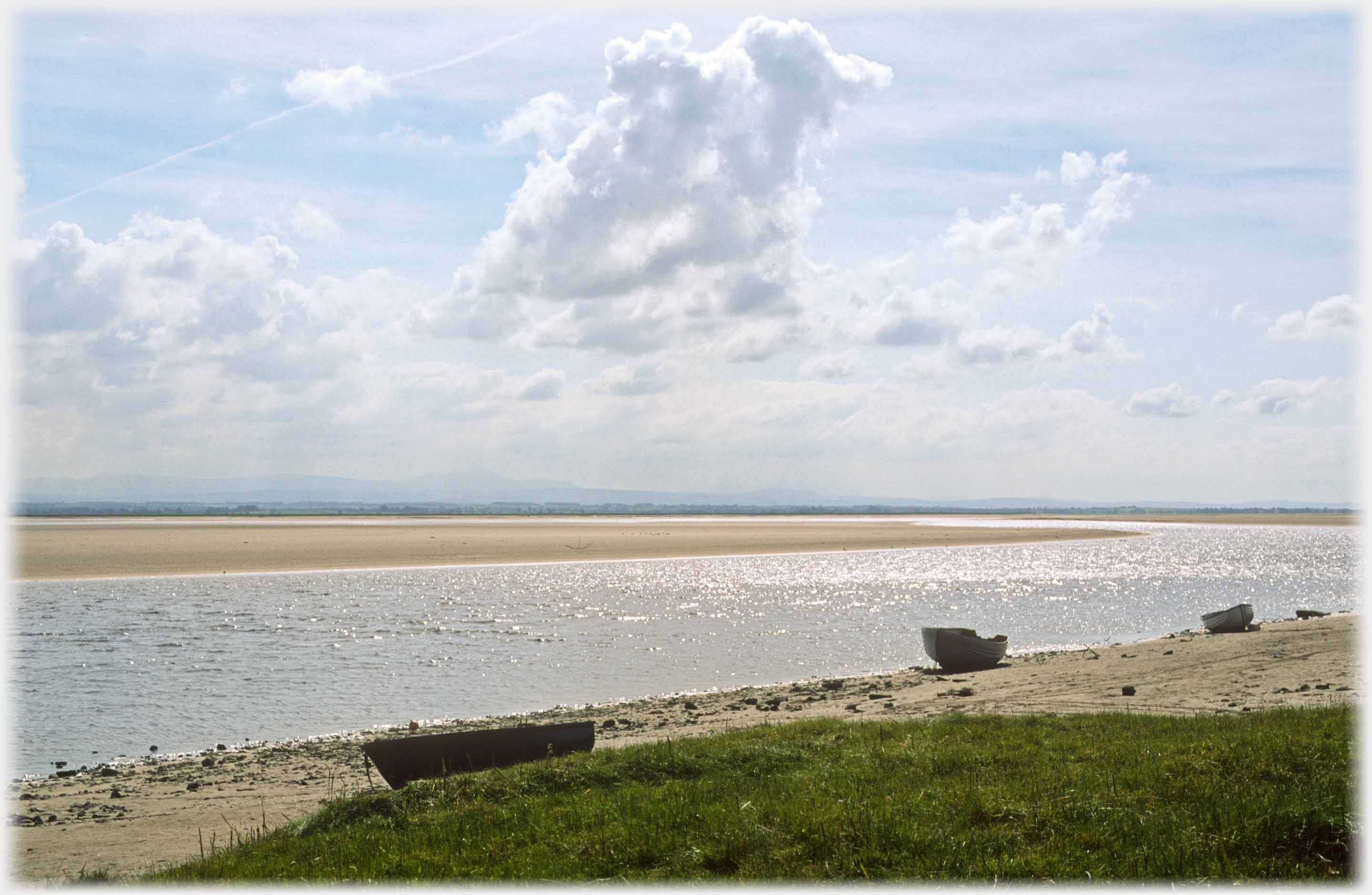 Three boats on beach by water, upper half clouds.