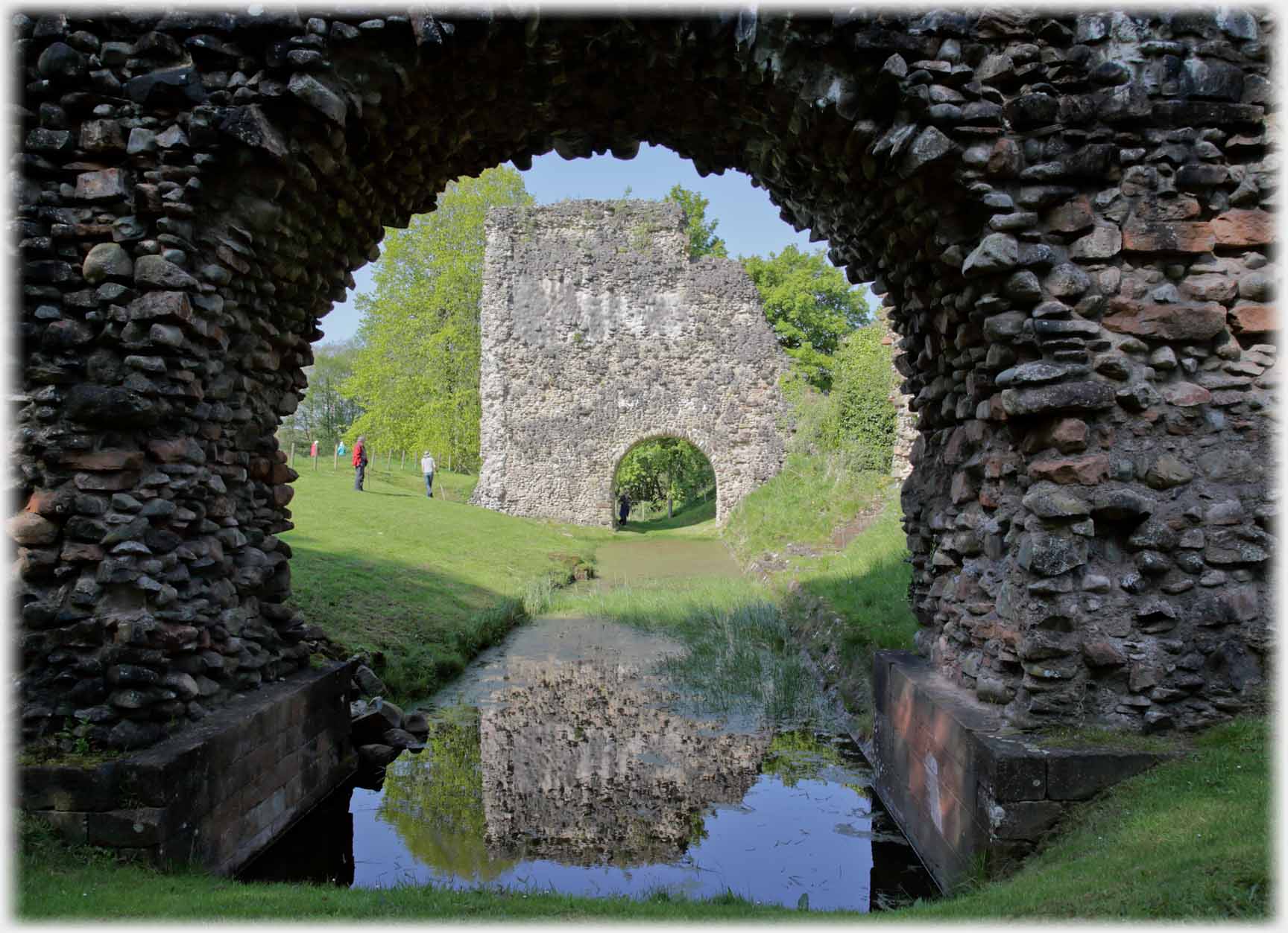 Looking through stone arch over pool, part of wall with arch further along.