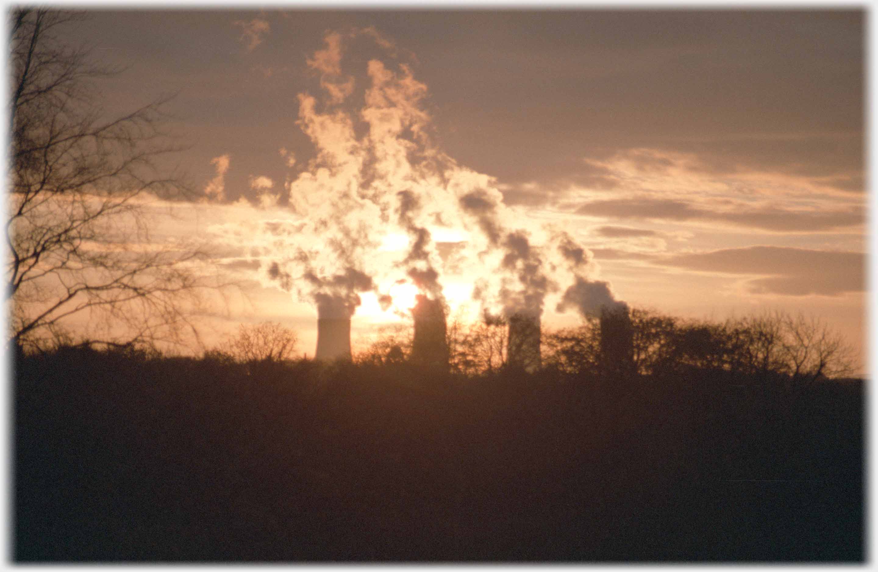 Four cooling chimneys steaming in sunset, dark foreground.