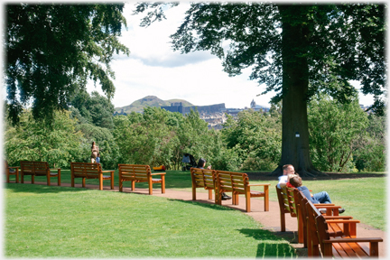 Path lined with benches, trees beyond and Arthur's Seat framed by them.