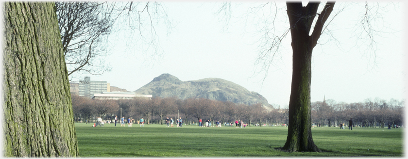Buildings and Arthur's Seat seen across an open grassed park.