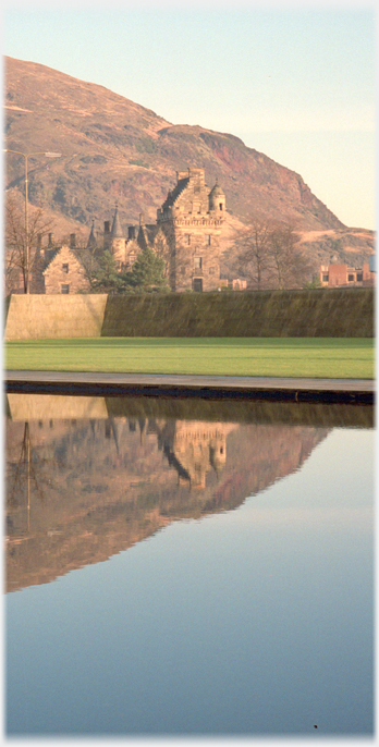 Building reflected in pool with part of hill behind.