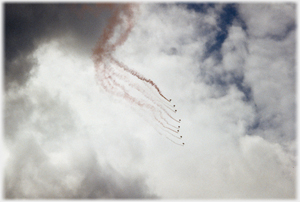 Team of sky divers with flares against clouds.