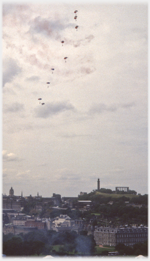 Team of sky divers with flares moving left-wards across sky.