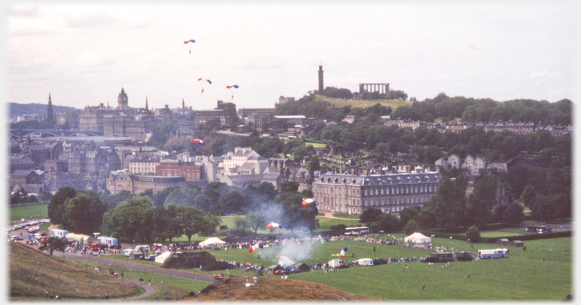 Tents and people around area beside the Palace with some sky divers landing, others following down.