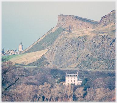 A large house appears isolated against a backdrop of rocks and crags.