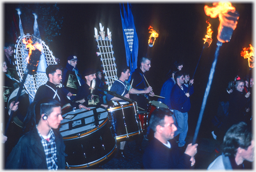 Drummers marching with torch bearers.