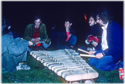 People watching the xylephone being played, a can of export to hand.