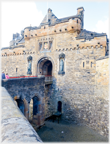 Bridge to small arched entrance in wall with two statues.