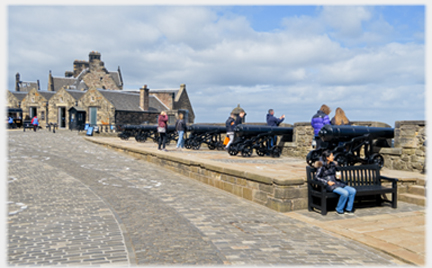 Line of cannons on low plinth, some vistors in view.