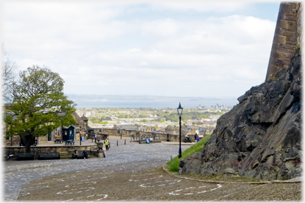 Looking down a broad curving cobbled road with city and sea beyond.