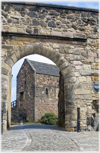 Stone arch in wall with end of building seen beyond.